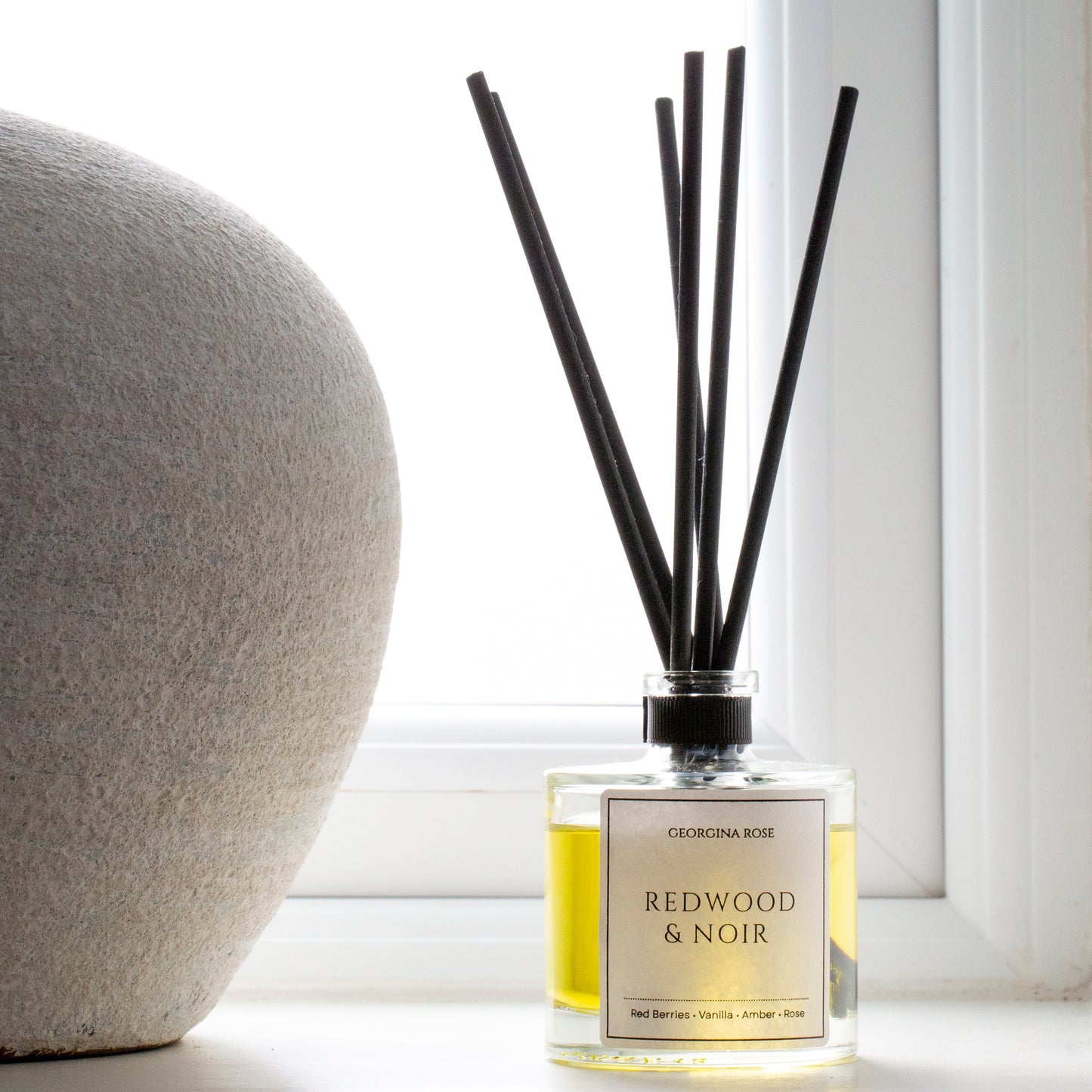 Diffuser bottle labeled 'Redwood & Noir' with black sticks on a light surface.