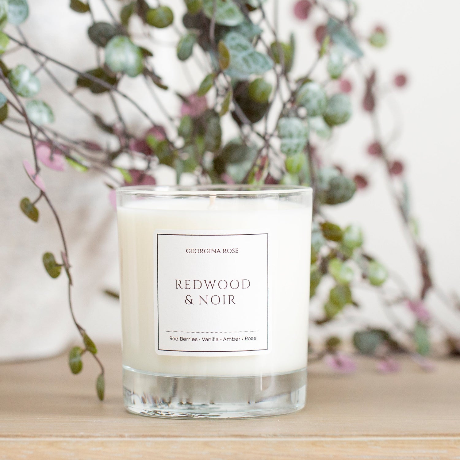 Candle labeled 'Redwood & Noir' with decorative branches in the background