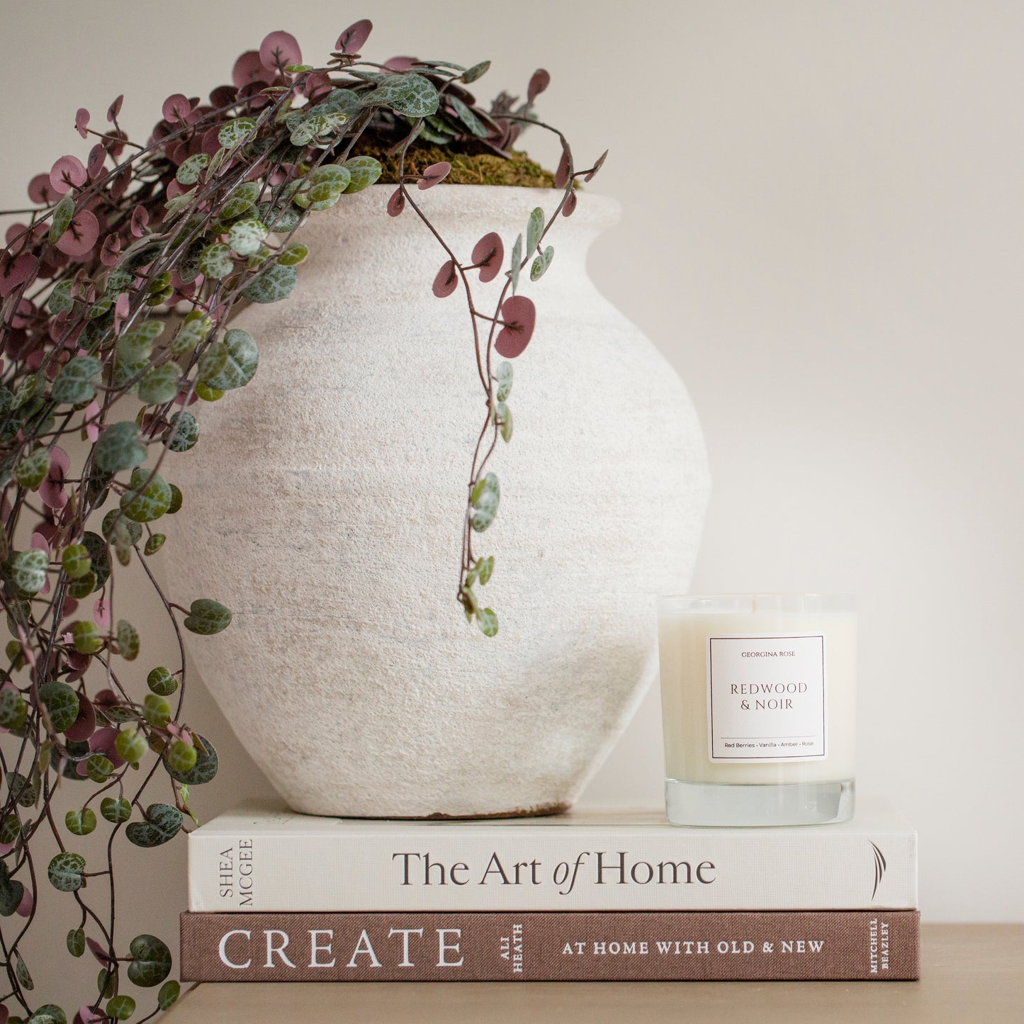 Decorative setup with a white vase, candle, and books on a neutral background