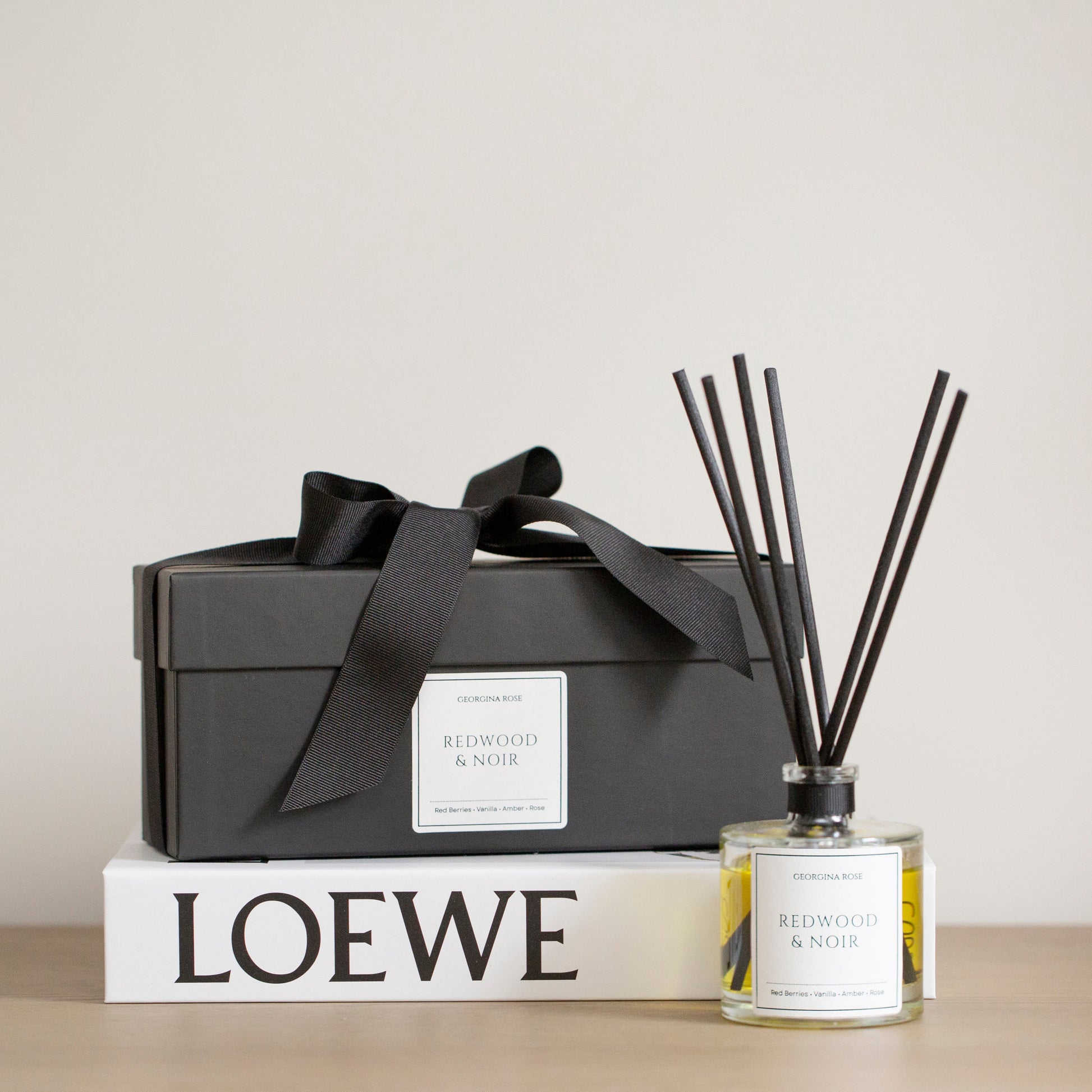 Reed diffuser with black sticks and a black box on a LOEWE book against a beige background