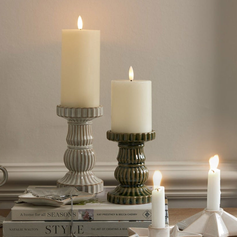 Candles in various holders on a wooden surface with a neutral background