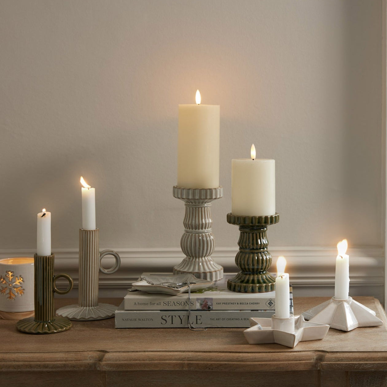 Candles in various holders on a wooden surface with a neutral background