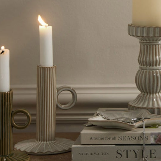 Candles in various holders on a wooden surface with a neutral background